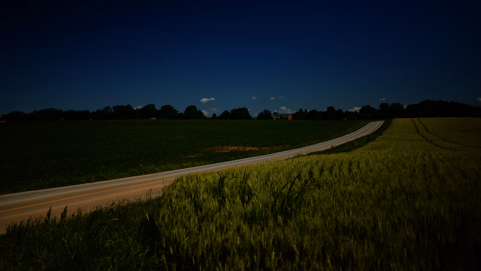 Country road winding through Kentucky farmland at dusk, white fences lining the path toward the horizon